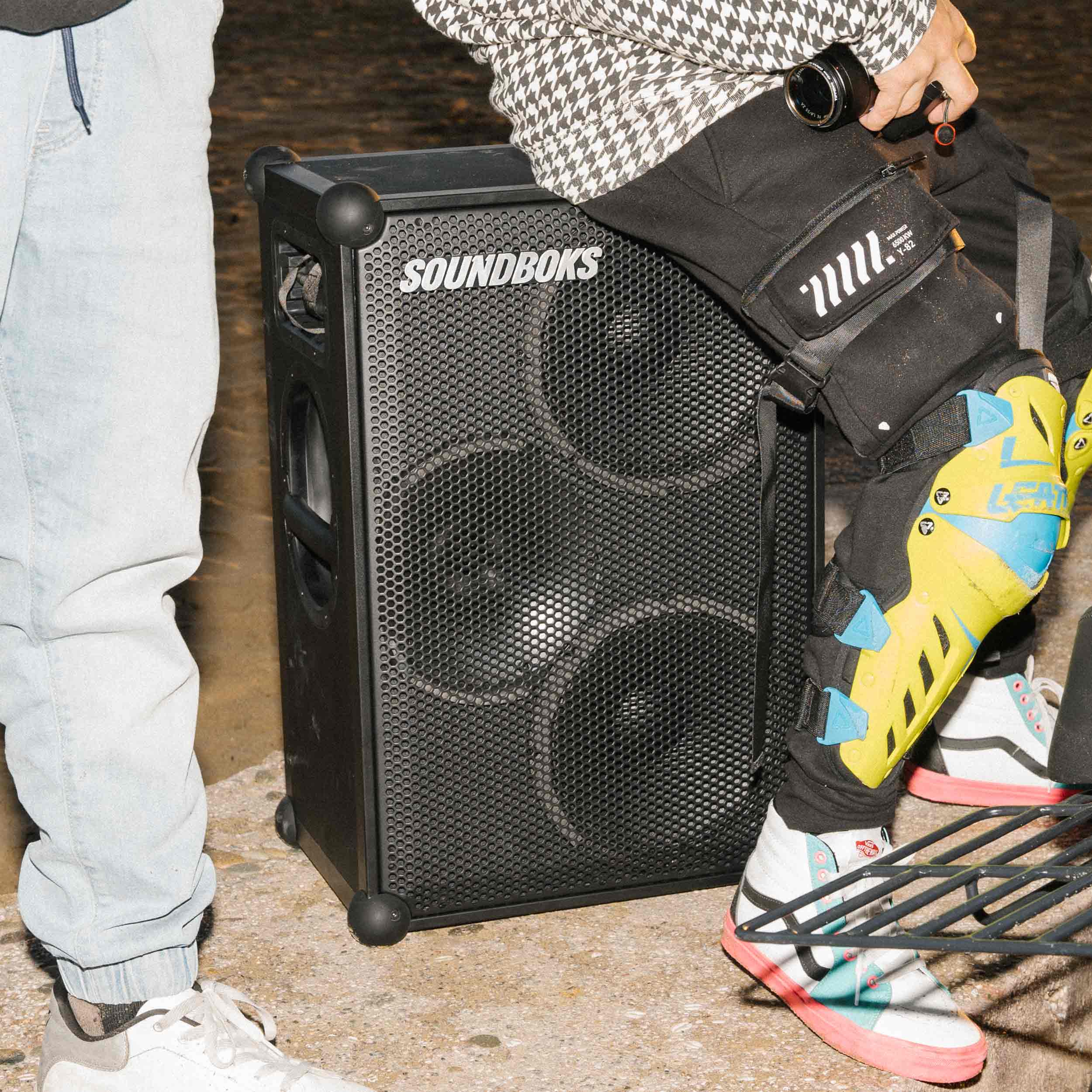 A person sits on a SOUNDBOKS 4 party speaker outdoors